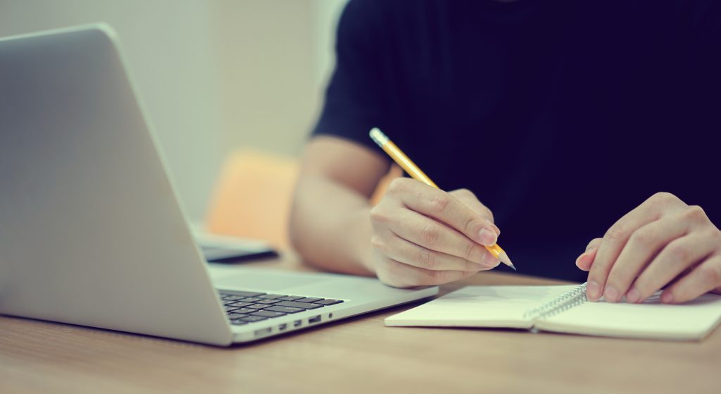 Jovem estudando com um computador e um caderno