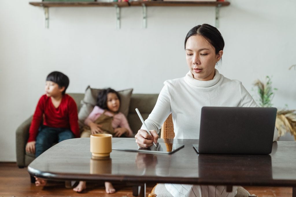 Mulher trabalha em casa com seus filhos ao fundo